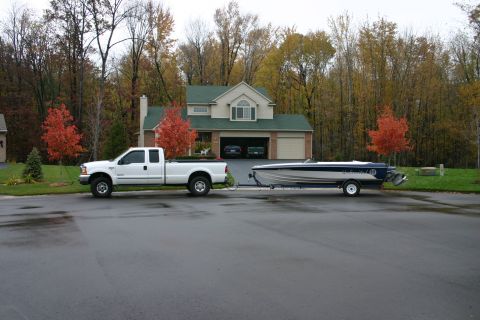 1999 Ford F-350 - A white 1999 Ford F-350 truck is parked on a wet street, towing a boat on a trailer in front of a suburban house.