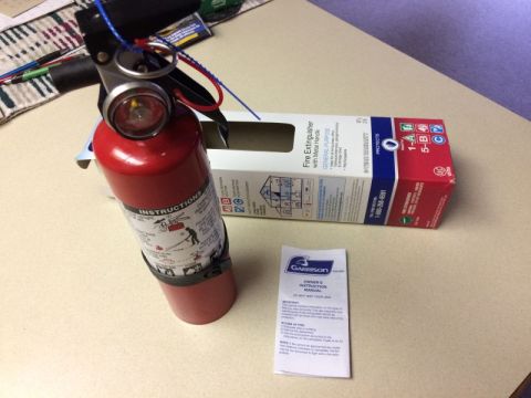2002 Pontiac Grand Prix - A red fire extinguisher and its box are shown on a table, along with an owner's instruction manual.
