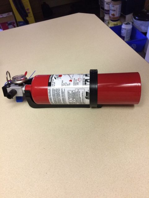 2002 Pontiac Grand Prix - A red fire extinguisher is mounted on a black bracket on a light-colored surface. The fire extinguisher has instructions printed on its sid…