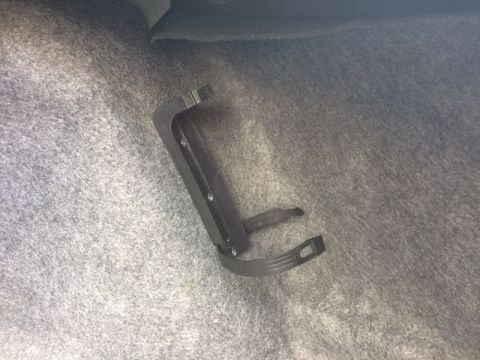 2002 Pontiac Grand Prix - A black plastic bracket is mounted to the gray carpeted floor of a vehicle trunk. The bracket has several small screws visible and a strap…
