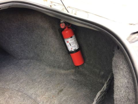 2002 Pontiac Grand Prix - A red fire extinguisher is mounted inside the trunk of a car, secured to the carpeted wall with a black bracket.