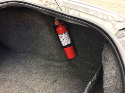 2002 Pontiac Grand Prix - A red fire extinguisher is mounted inside the trunk of a car with gray carpet lining. The fire extinguisher is secured to the upper left si…