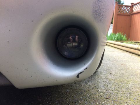 2002 Pontiac Grand Prix - A close-up, low-angle view of the driver's side fog light assembly on a silver car bumper. The fog light lens is dark and reflects a person…