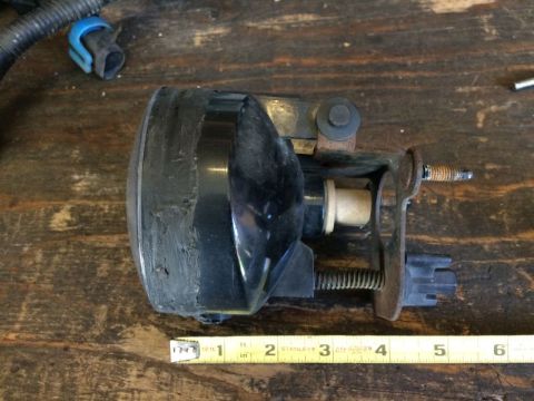 2002 Pontiac Grand Prix - A black headlight assembly with a rusty metal bracket is shown on a wooden surface. A yellow measuring tape is visible along the bottom edg…