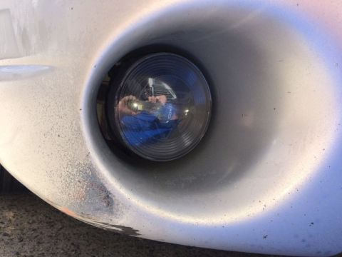 2002 Pontiac Grand Prix - Close-up view of a fog light housing on the front bumper of a silver vehicle. The fog light lens is dark and reflects a person wearing a bl…