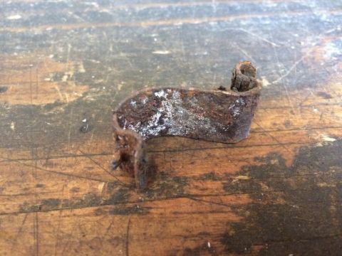 2002 Pontiac Grand Prix - A rusty metal bracket is shown resting on a wooden surface. The bracket is curved and shows signs of significant corrosion and wear.