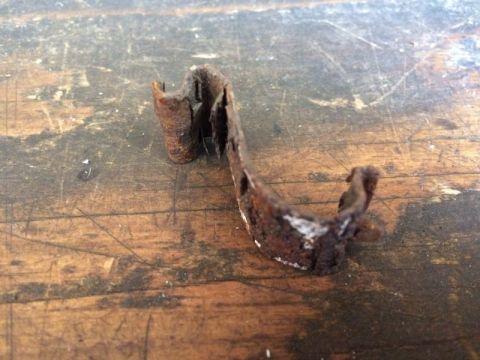 2002 Pontiac Grand Prix - A heavily rusted and bent metal bracket is shown resting on a worn wooden surface. The bracket appears to be a small, irregularly shaped co…