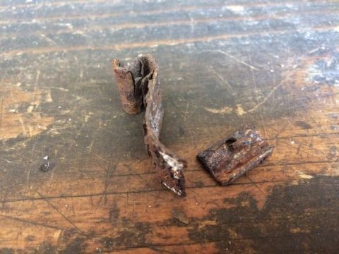 2002 Pontiac Grand Prix - Two small, rusted metal fragments are lying on a weathered wooden surface. One fragment is curved and elongated, while the other is a small…