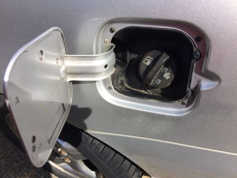 2002 Pontiac Grand Prix - The image shows an open fuel filler door on a silver car, revealing the fuel cap. The fuel cap has symbols indicating fuel type and a lock.