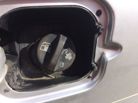2002 Pontiac Grand Prix - A close-up view of the fuel filler door and cap on a silver vehicle. The cap has symbols indicating fuel and emissions.