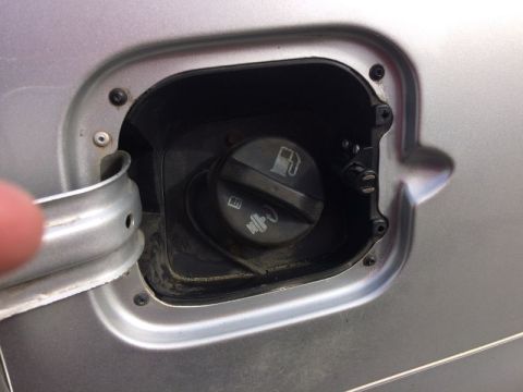 2002 Pontiac Grand Prix - A close-up view of an open fuel filler door on a silver car, revealing the gas cap and surrounding mechanism. The fuel door is detached and…