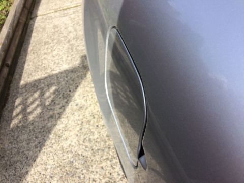 2002 Pontiac Grand Prix - A close-up, side view of a silver Pontiac Grand Prix's fuel door. The car is parked on a concrete driveway next to a wooden border.