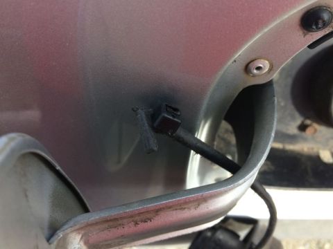 2002 Pontiac Grand Prix - A close-up view shows a black plastic clip attached to a dark wire, mounted on the exterior body panel of a vehicle near the fuel filler do…