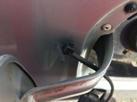 2002 Pontiac Grand Prix - A close-up view of a black plastic clip attached to a dark grey cable, which is mounted on the exterior body panel of a vehicle near the fu…