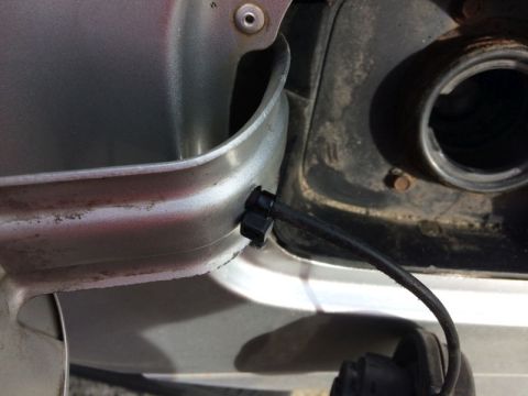2002 Pontiac Grand Prix - A close-up view of a black fuel filler neck hose attached to the fuel door of a silver vehicle. The hose is secured with a black clip to th…