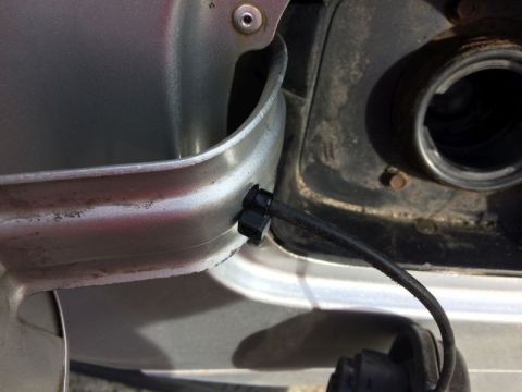 2002 Pontiac Grand Prix - A close-up view shows a black cable attached to a clip on the edge of a silver car's fuel filler door. The cable extends towards the open f…