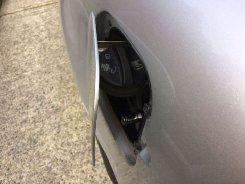 2002 Pontiac Grand Prix - A close-up view of an open silver fuel filler door on a car, revealing the black gas cap with symbols. The car is parked on a concrete surf…