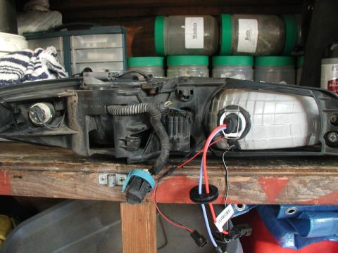 2002 Pontiac Grand Prix - A disassembled headlight assembly for a 2002 Pontiac Grand Prix is shown on a wooden workbench. Wires and a bulb socket are connected to th…