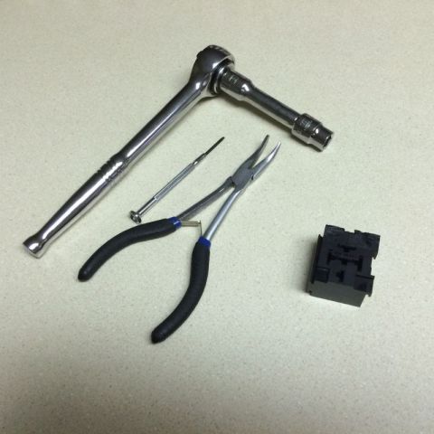 2002 Pontiac Grand Prix - A collection of tools including a ratchet, needle-nose pliers, a small screwdriver, and a black electrical component are laid out on a spec…