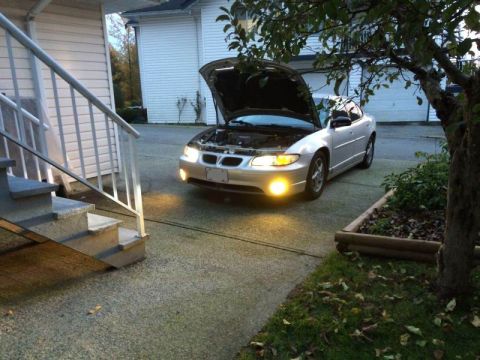 2002 Pontiac Grand Prix - A silver Pontiac Grand Prix with its hood open is parked in a driveway. The car's headlights and fog lights are illuminated.