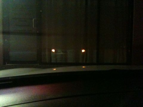 2002 Pontiac Grand Prix - The headlights of a car are visible through a glass window at night. The reflection on the glass shows a dark interior and a door handle.