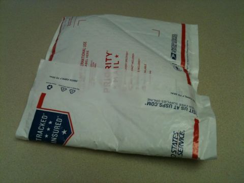2002 Pontiac Grand Prix - Two white USPS Priority Mail envelopes are stacked on a textured surface. The top envelope is partially covering the bottom one, and both h…