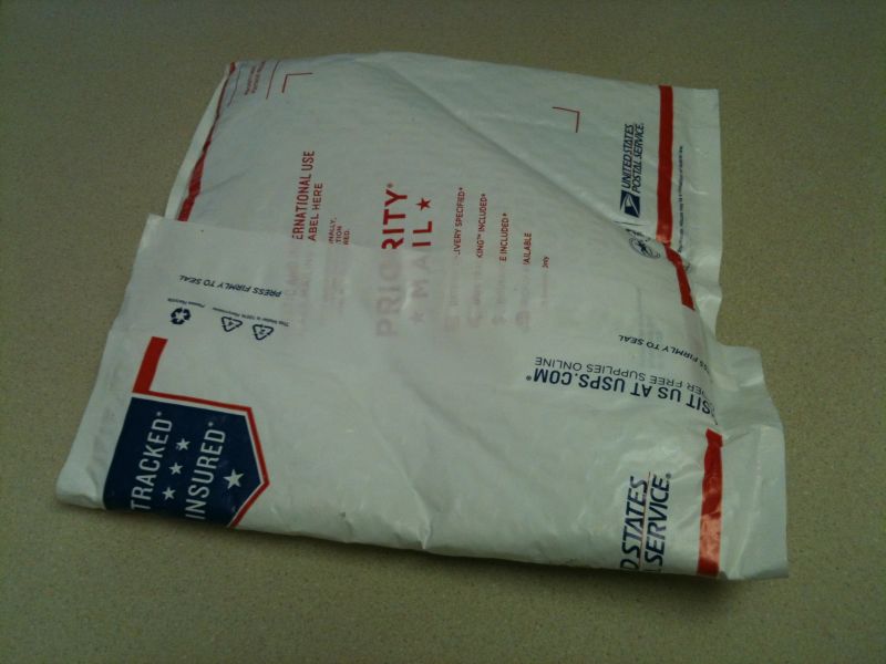 Two white USPS Priority Mail envelopes stacked on a textured surface.