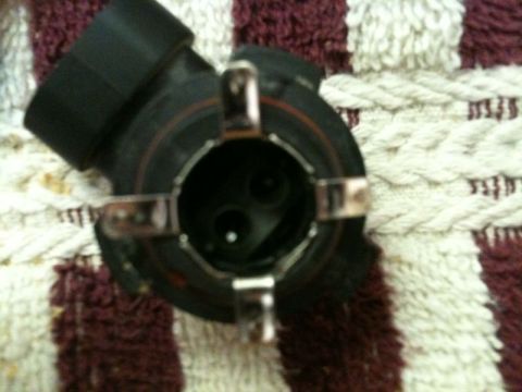 2002 Pontiac Grand Prix - This is a close-up, top-down view of a black automotive headlight bulb socket with metal retaining clips. The socket is resting on a textur…