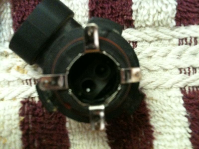 Black headlight bulb socket with metal clips on a striped fabric surface.
