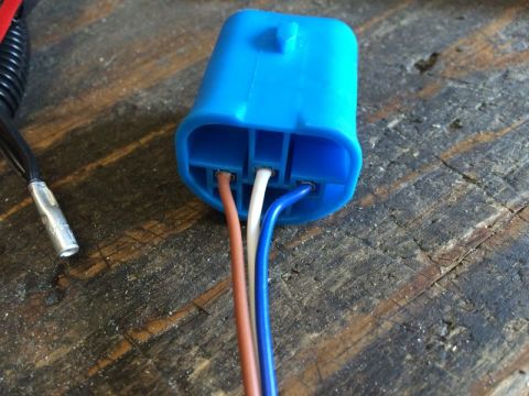 2002 Pontiac Grand Prix - A close-up view of a blue electrical connector with three wires (brown, white, and blue) inserted into it. A black wire with a metal termin…