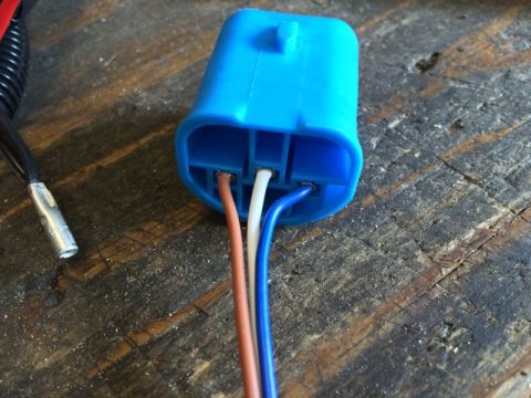 2002 Pontiac Grand Prix - A close-up view of a blue electrical connector with three wires (brown, white, and blue) inserted into it, resting on a weathered wooden su…