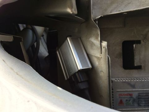 2002 Pontiac Grand Prix - A close-up view shows a silver ballast with fins and a black connector attached to a vehicle's metal frame. Text on a silver plate below th…