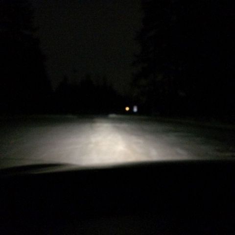 2002 Pontiac Grand Prix - The headlights of a vehicle illuminate a dark, snowy road at night. Two distant lights are visible ahead.