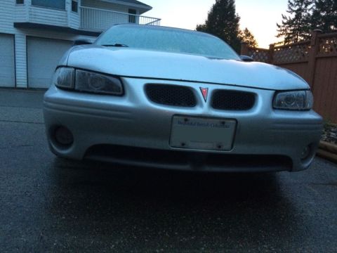 2002 Pontiac Grand Prix - The front view of a silver Pontiac Grand Prix is shown parked on a wet asphalt driveway in front of a house. The car has a license plate th…