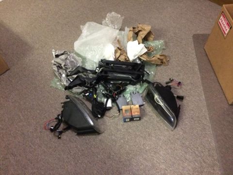 2002 Pontiac Grand Prix - A pile of car parts, including headlights, wiring harnesses, and control modules, are laid out on a carpeted floor next to a cardboard box…