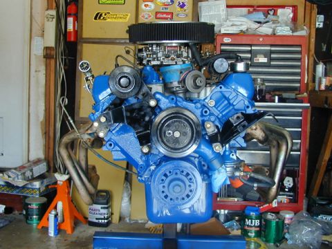 1979 Ford Bronco - A blue V8 engine assembly is displayed on a stand, surrounded by garage equipment and workshop items.