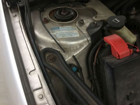 2002 Pontiac Grand Prix - A close-up view of the engine bay of a 2002 Pontiac Grand Prix, focusing on the battery and surrounding components. A blue sticker with whi…