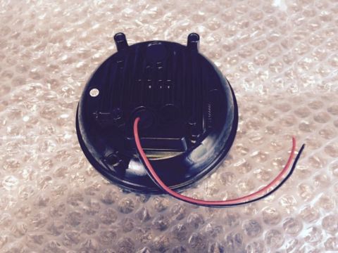 2002 Pontiac Grand Prix - The back of a black, round LED headlight assembly with red and black wires protruding from it. The assembly is resting on a surface covered…