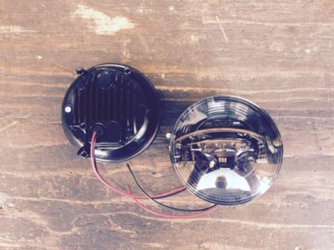 2002 Pontiac Grand Prix - Two round LED headlights are shown from a top-down perspective on a wooden surface. One headlight is black with visible heat sinks and wire…