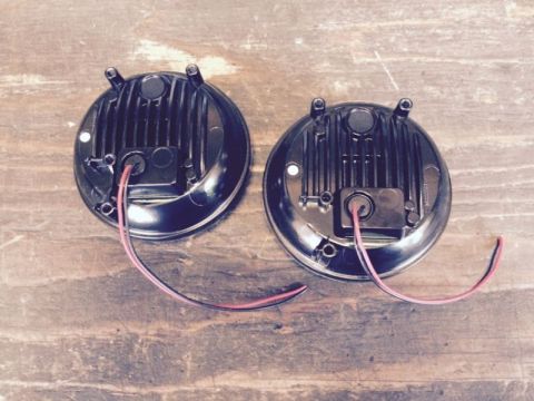 2002 Pontiac Grand Prix - The rear view of two round black LED lights with red and black wires attached, resting on a wooden surface.