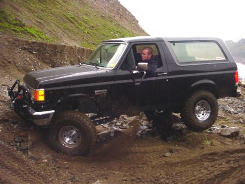1988 Ford Bronco - A black Ford Bronco navigates a challenging off-road terrain with a driver behind the wheel.