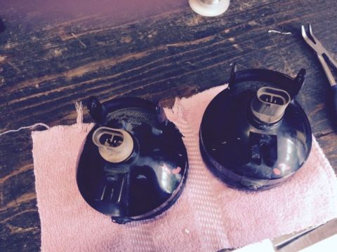 2002 Pontiac Grand Prix - Two black fog light assemblies are shown resting on a pink towel on a wooden surface. The assemblies have electrical connectors visible at…