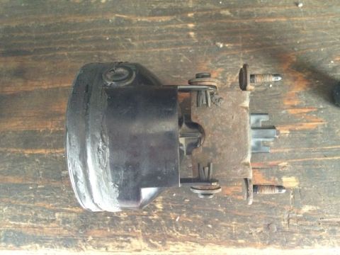 2002 Pontiac Grand Prix - A close-up side view of a black automotive lighting component, possibly a fog light, mounted on a rusty metal bracket with two visible scre…