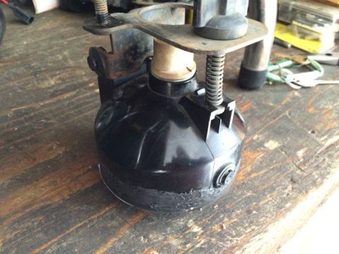 2002 Pontiac Grand Prix - A close-up view of a black automotive part, possibly a headlight assembly, mounted on a wooden surface. The part shows signs of wear and mo…