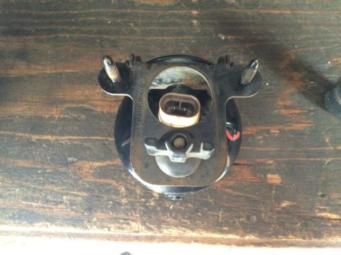 2002 Pontiac Grand Prix - A black automotive fog light assembly is shown mounted on a wooden surface. The assembly has a metal bracket with two threaded posts and a…