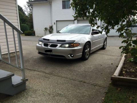 2002 Pontiac Grand Prix - A silver Pontiac Grand Prix with a black bug deflector is parked on a concrete driveway in front of a house. The car is viewed from a front…