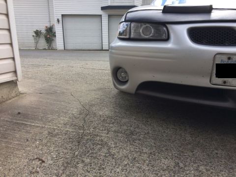 2002 Pontiac Grand Prix - A close-up, low-angle shot of the front bumper and headlight of a silver Pontiac Grand Prix. The car is parked on a cracked concrete drivew…
