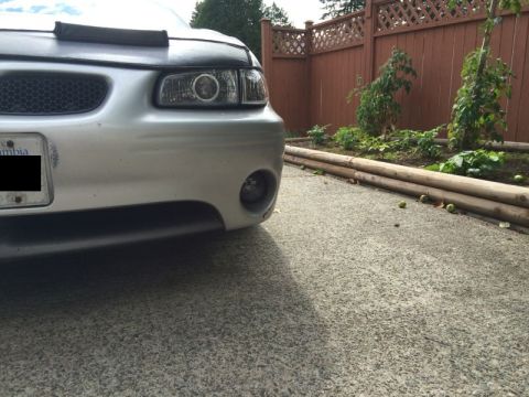 2002 Pontiac Grand Prix - The front driver's side quarter of a silver Pontiac Grand Prix is shown parked on a concrete driveway. A black car bra covers the hood, and…