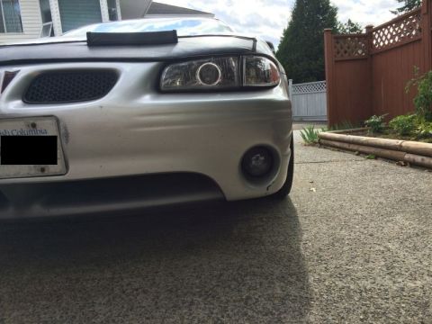2002 Pontiac Grand Prix - Front view of a silver Pontiac Grand Prix with a black bra on the hood. The vehicle is parked on a concrete driveway next to a garden with…