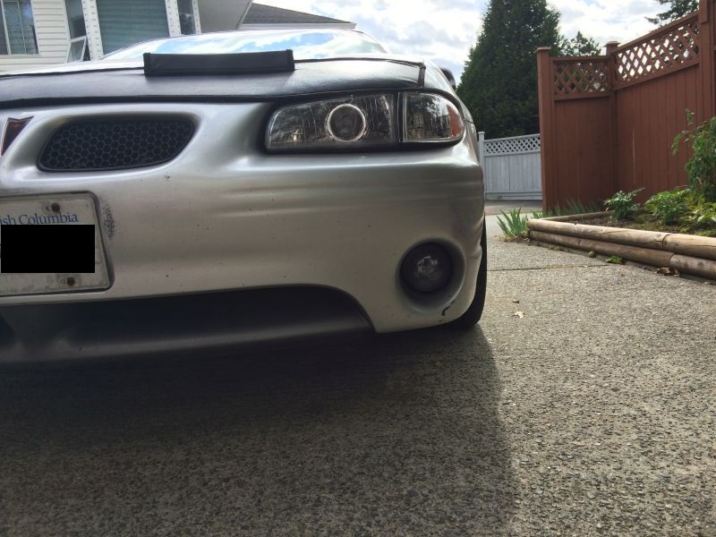 Silver Pontiac Grand Prix front view with black bra on hood, parked on driveway.